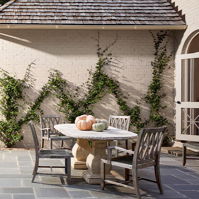 Cette maison en briques de couleur blanche imprégnée d’un soupçon de pêche avec des vignes grimpantes présente un spacieux patio en ardoise avec un coin à manger comportant une table en pierre et des chaises en bois.