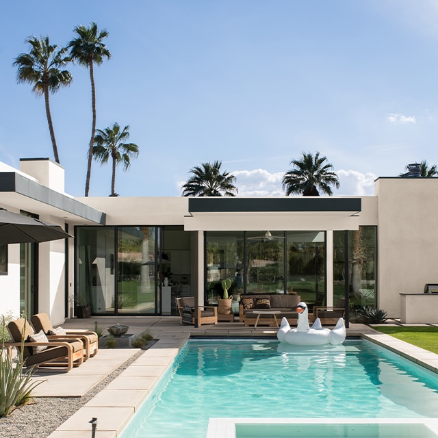 Maison moderne en stucco blanc avec moulures noires, palmiers à l’arrière et magnifique cour avec piscine et patio.
